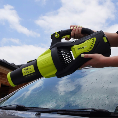 Person using a BlowR CHARGD on a car's windshield with a clear sky background